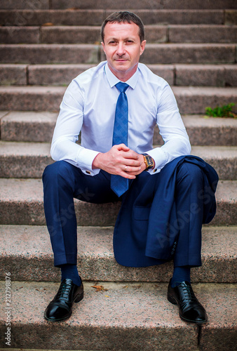 Stylish man in white shirt and tie, sits on stone staircase
