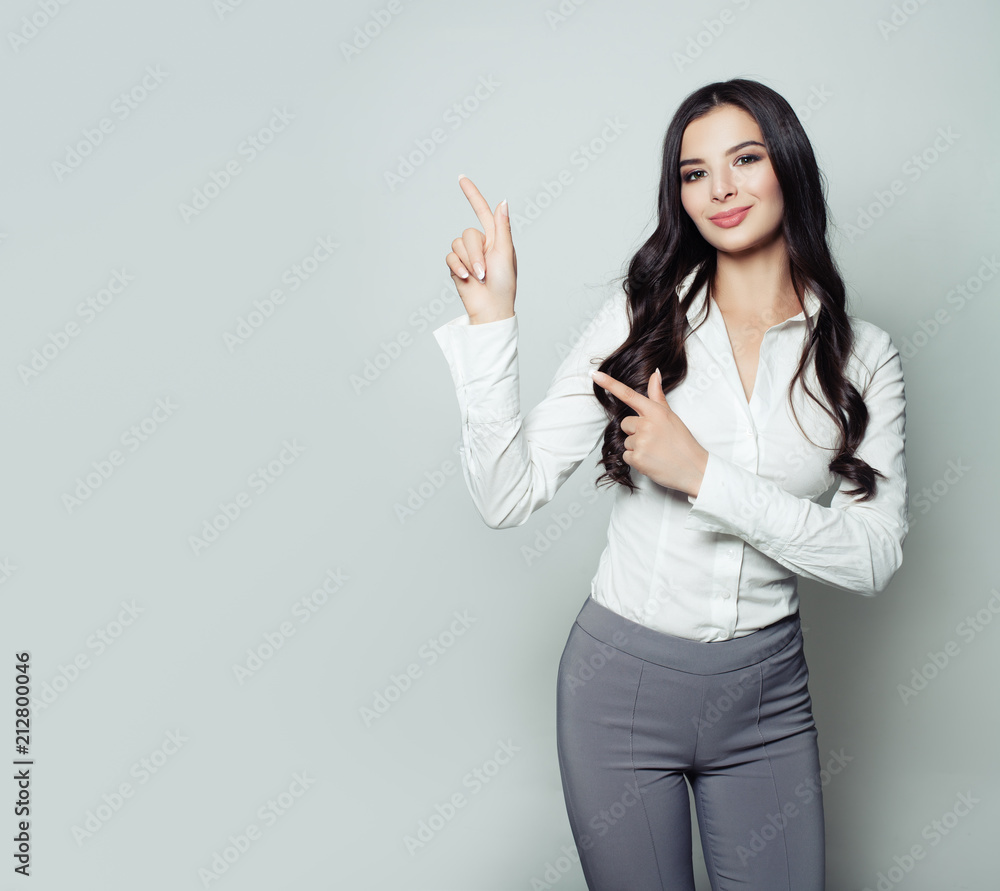 Young business woman pointing her finger up on gray background with copy space. Friendly woman portrait, advertising marketing and product placement concept Young business woman pointing her finger up on gray background with copy space. Friendly woman portrait, advertising marketing and product placement concept