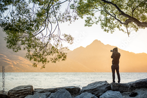 Young male photographer looking at scenery of Lake Wakatipu during golden hour sunset in Queenstown, South island, New Zealand, travel and landscape photography concepts photo