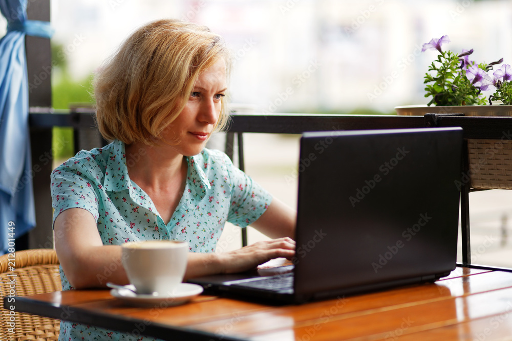 Woman is sitting at the table with a laptop and a cup of coffee Woman is sitting at the table with a laptop and a cup of coffee