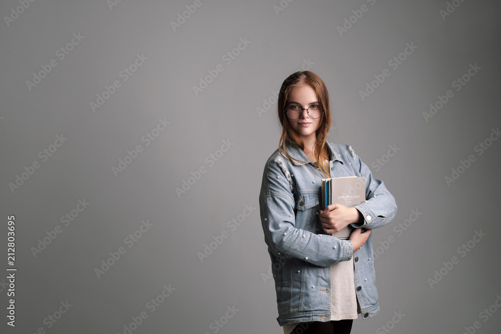 Beautiful young girl student in a jeans jacket holds notebooks and textbooks on a gray background. Beautiful young girl student in a jeans jacket holds notebooks and textbooks on a gray background.