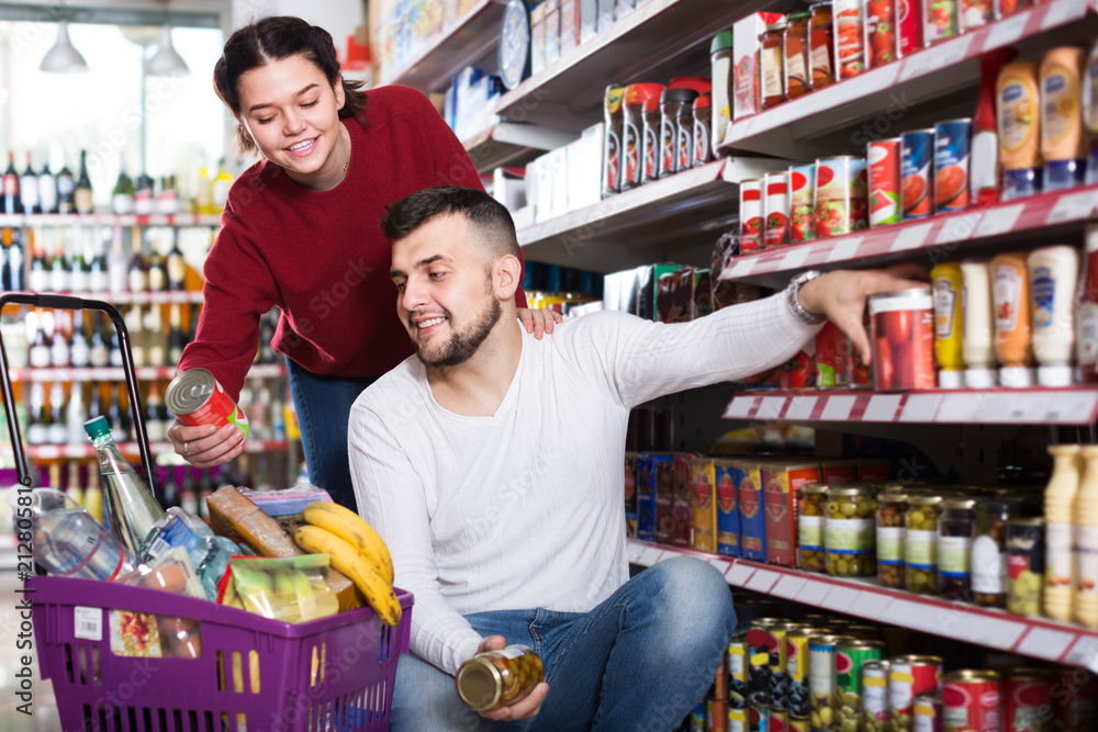 vigorous couple choosing purchasing canned food for week at supermarket
