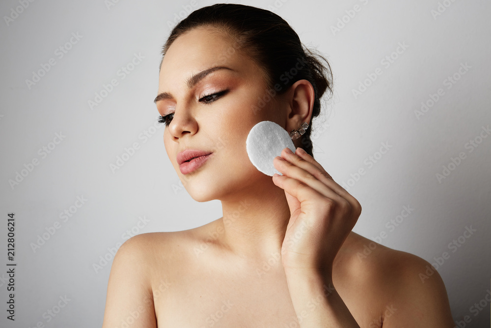 Beautiful girl with big brown eyes and dark eyebrows refreshing skin face with cotton pads over gray studio background.Model with light nude make-up.Healthcare skin makeup concept Beautiful girl with big brown eyes and dark eyebrows refreshing skin face with cotton pads over gray studio background.Model with light nude make-up.Healthcare skin makeup concept