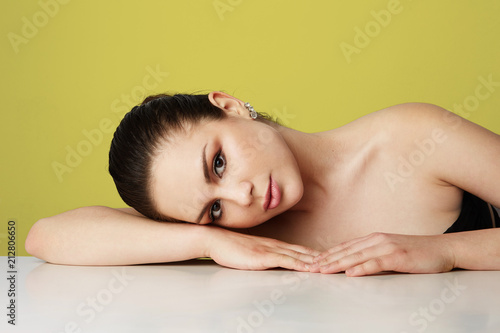 Beautiful young woman with big brown eyes and dark eyebrows relaxing over empty yellow studio background.Model with light nude make-up.Copy paste space,close up.Healthcare skin concept
