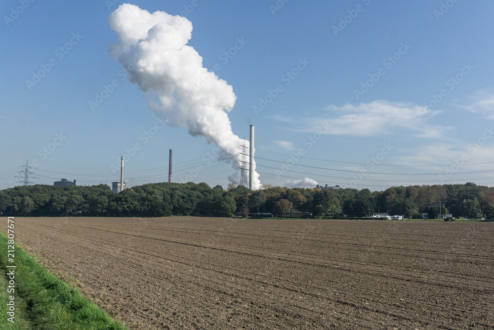View of the cleaned empty field by the town with smoking pipes of the plant View of the cleaned empty field by the town with smoking pipes of the plant
