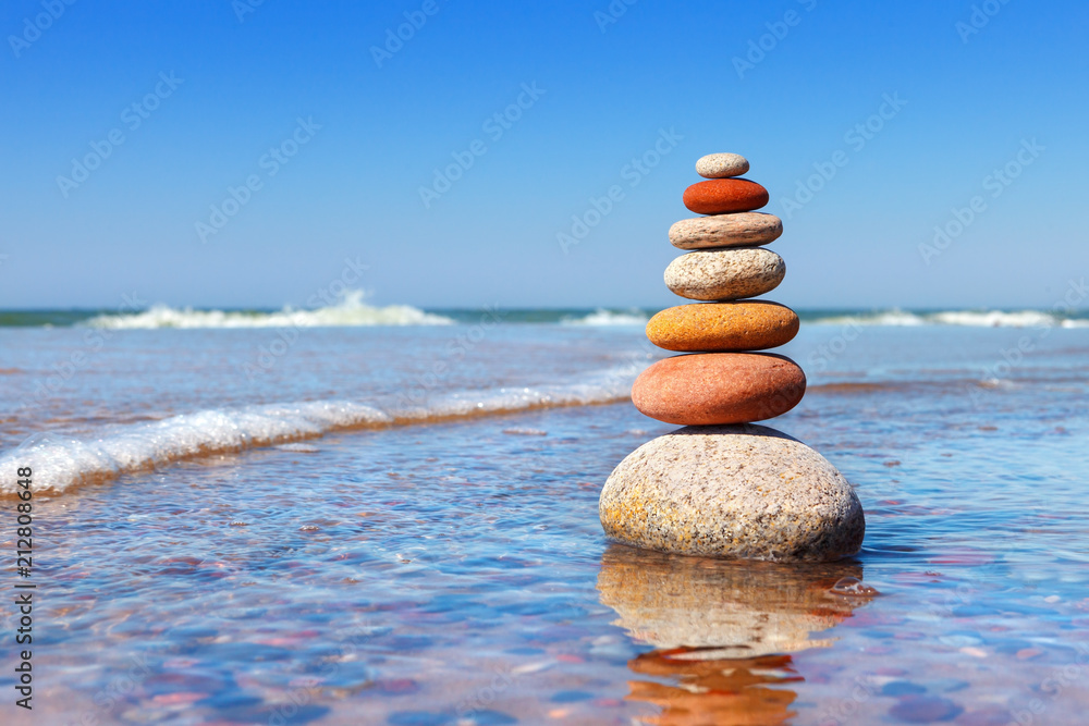 Rock zen pyramid of colorful pebbles standing in the water on the background of the sea. Concept of balance, harmony and meditation. - obrazy, fototapety, plakaty 