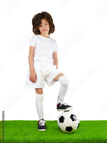 Young European boy, fan or player in white uniform with soccer ball standing on green grass, cheer favorite football team. Sport play football, lifestyle concept. Isolated on white