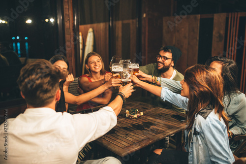 Group of friends drink beer on the terrace and toast during summer night