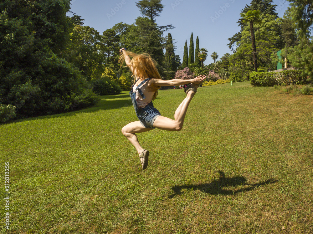 Girl dancer doing a beautiful jumping movement on green grass