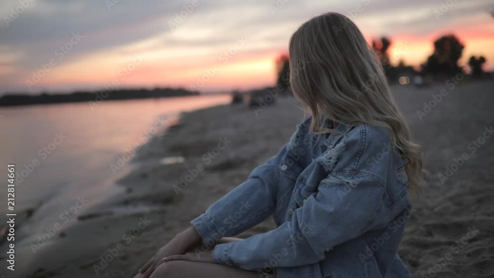 Young woman sitting on river beach at sunset looking around and dreaming Young woman sitting on river beach at sunset looking around and dreaming
