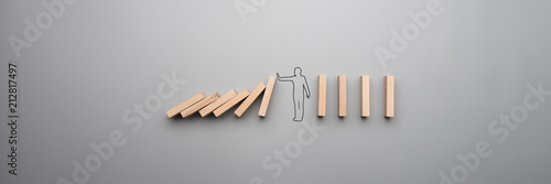 Wide cropped image of the outline of a businessman stopping the domino photo