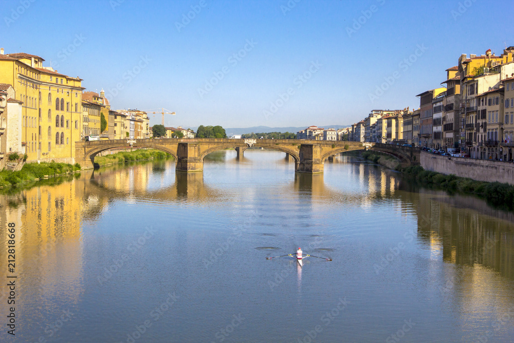 Panoramic view of the Arno River and stone medieval bridge Ponte Vecchio with beautiful reflection of colorful houses and small boat, Florence, Tuscany, Italy.