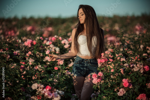Happy smiling woman is resting in blossom garden of beautiful pink roses