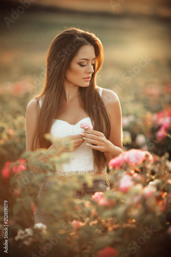 Happy smiling woman is resting in pink blossom garden of beautiful roses over sunset lights