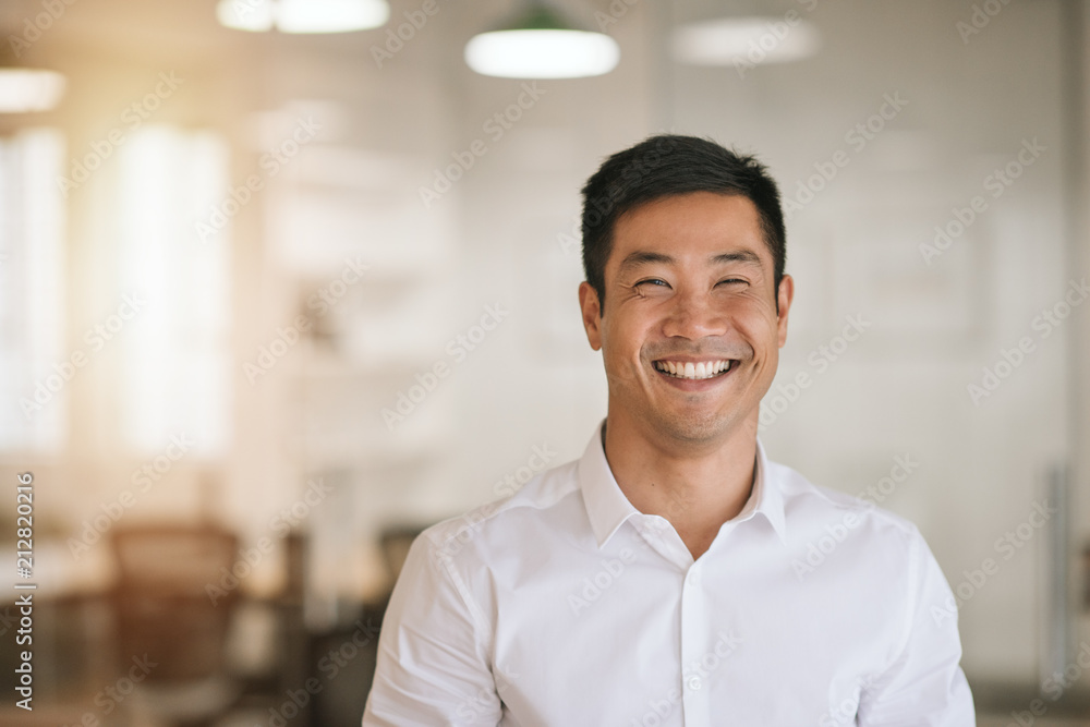 Smiling Asian businessman standing in a bright modern office Smiling Asian businessman standing in a bright modern office