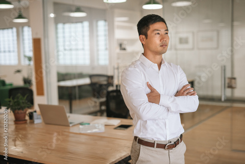 Focused Asian businessman standing in an office deep in thought