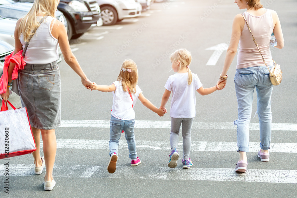 Group of four girl friends walking together through crosswalk . Two young woman with two daughters having fun outdoors near shopping mall. Children and adults friendship concept Group of four girl friends walking together through crosswalk . Two young woman with two daughters having fun outdoors near shopping mall. Children and adults friendship concept