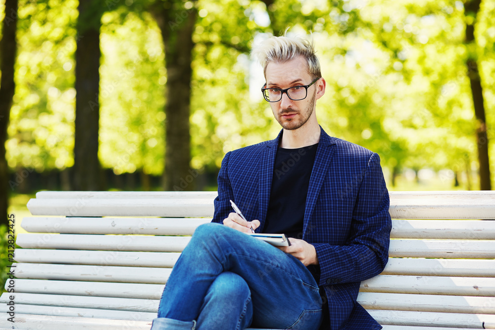 Creative male sitting on bench with notebook Creative male sitting on bench with notebook