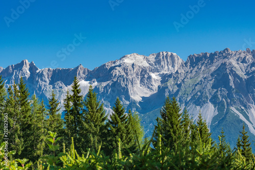 The summit Koppenkarstein in the Dachstein mountain range in Austria with green trees in foreground photo