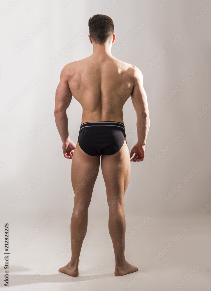 Rearview of handsome shirtless muscular man, standing, in studio shot, on white