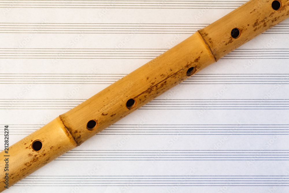 Naklejka premium Simple wooden flute on a background of pure sheet music