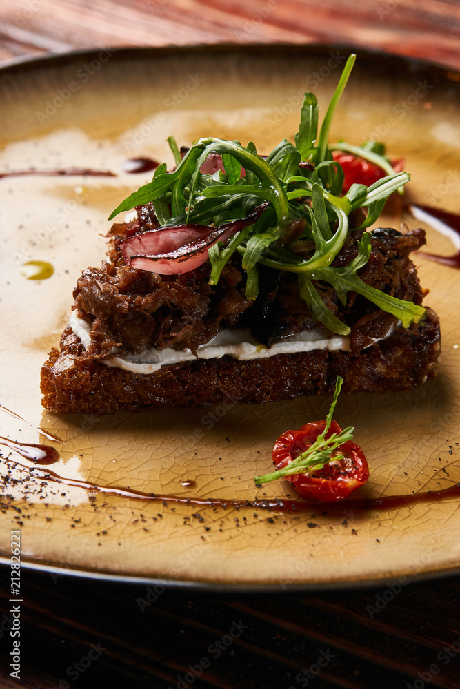 Fresh Bruschetta with lamb beef. Open sandwich with Dark rye bread, dried cherry tomatoes, rosemary, olives and arugula on plate at luxury restaurant table, top view. Delicious snack food Fresh Bruschetta with lamb beef. Open sandwich with Dark rye bread, dried cherry tomatoes, rosemary, olives and arugula on plate at luxury restaurant table, top view. Delicious snack food