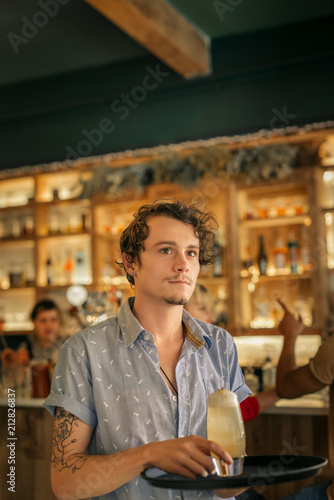 Young waiter serving cocktails in a trendy bar