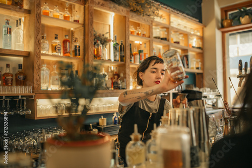 Foto Young female bartender pouring cocktails behind a bar counter