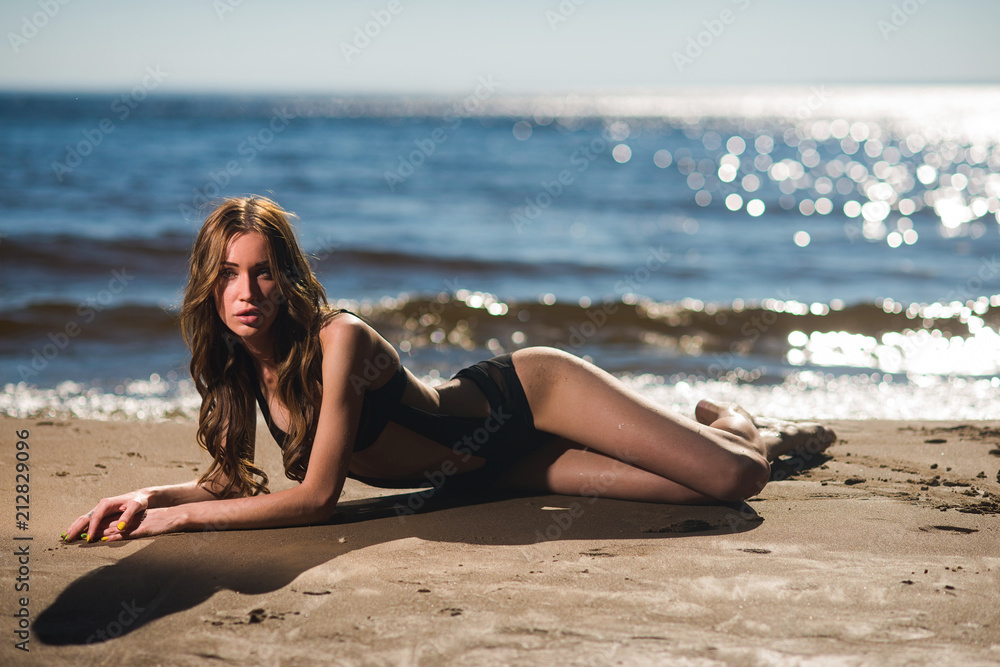 Beautiful sexy girl in a swimsuit lying on the beach against the sea