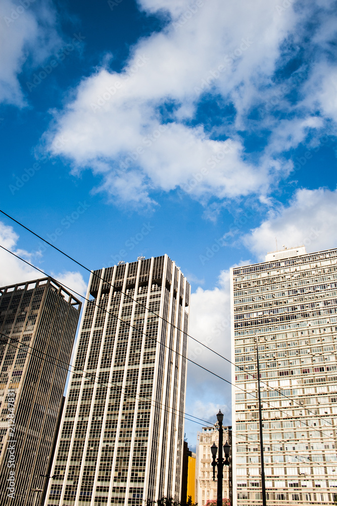Fototapeta premium An electric wire passes by this vertical image of business buildings in a blue sky with clouds day