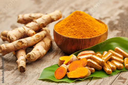 Turmeric powder in wooden bowls and turmeric capsules on wooden background photo