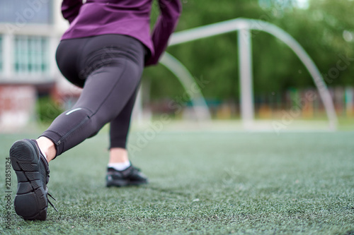 Woman stretching. Young female workout before fitness training session on a football field. Healthy young woman warming up outdoors.