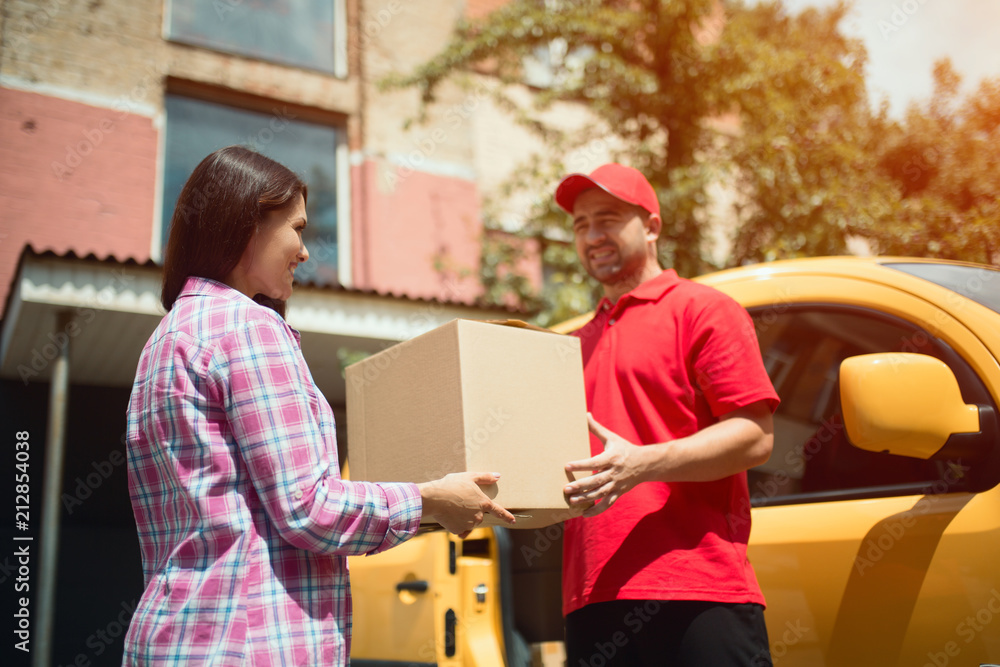 Man giving woman big delivery box. Cheerful delivery man handing big tan package to beautiful female customer. Man giving woman big delivery box. Cheerful delivery man handing big tan package to beautiful female customer.