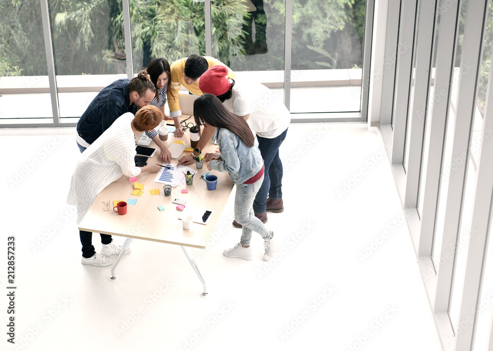 Group of business persons standing around a desk brainstorming and discussing work at the office .