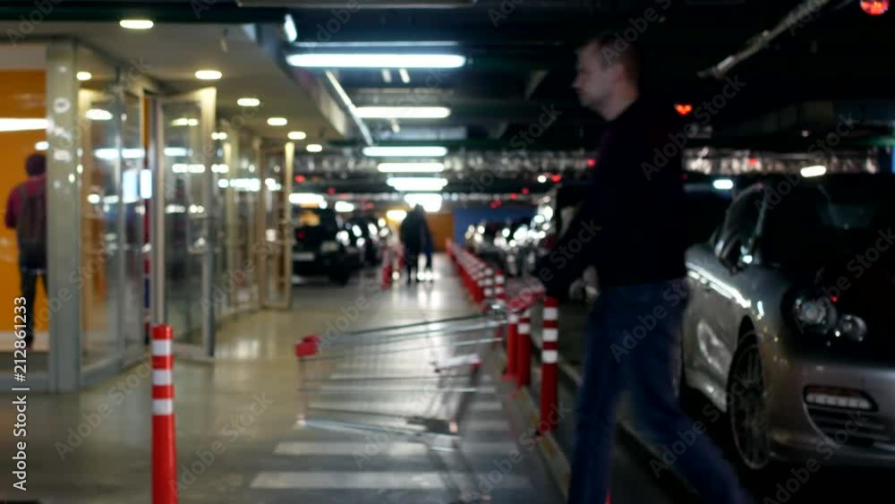 A young man with a cart goes on an underground car parking for shopping in a shopping center, concept A young man with a cart goes on an underground car parking for shopping in a shopping center, concept
