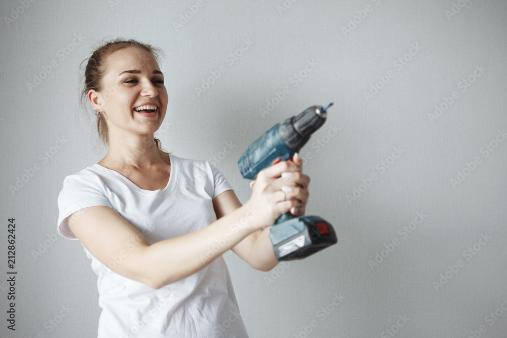 Young beautiful woman in a white T-shirt posing with a drill in a new apartment during a renovation. The concept of equality of women. Young beautiful woman in a white T-shirt posing with a drill in a new apartment during a renovation. The concept of equality of women.