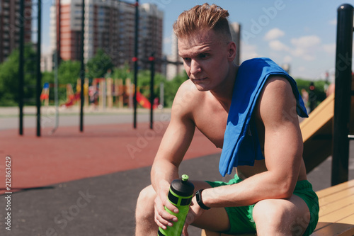 Fototapeta Naklejka Na Ścianę i Meble -  The inflated Athlete after training sits on the Playground with a towel on his shoulder