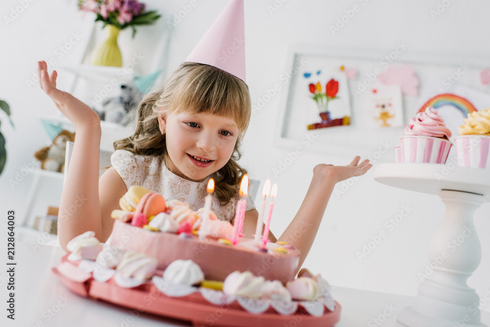 smiling little child with wide arms looking at birthday cake with candles smiling little child with wide arms looking at birthday cake with candles