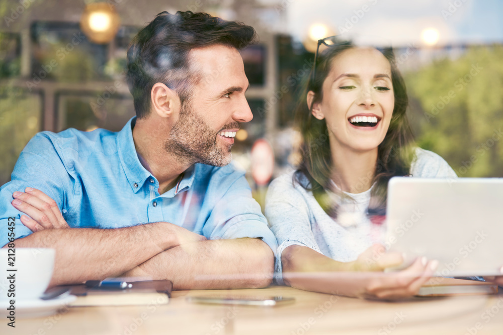 Couple sitting together in cafe looking at tablet and laughing Couple sitting together in cafe looking at tablet and laughing