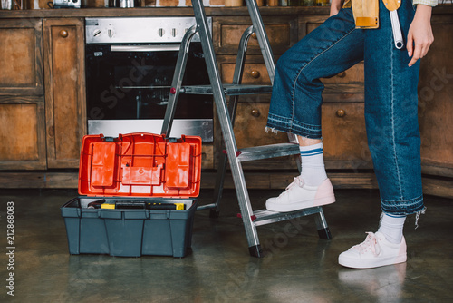 Fotografija cropped shot of repairwoman in jeans standing on stepladder at kitchen