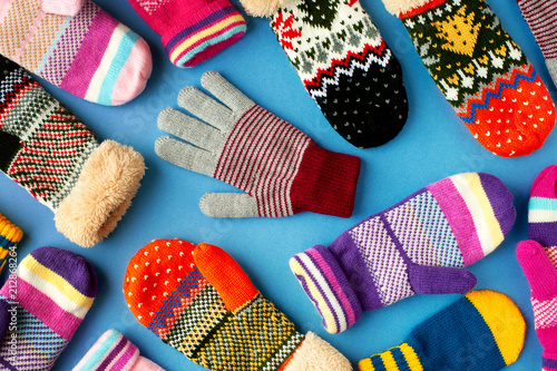 Mittens and gloves are scattered on the table. Multicolored mittens and gloves for autumn and winter. Clothes for the cold seasons on a blue background. View from above.