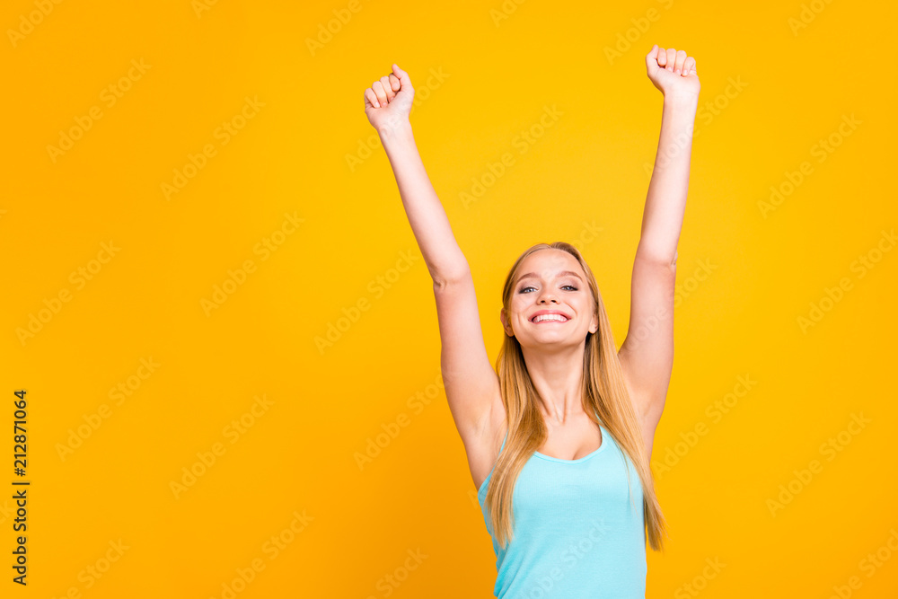 Happy young girl in blue t-shirt raised her hands up and looked happy at the camera high held head and make big smile. Yellow background with copy space