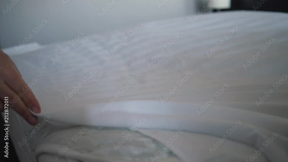 The girl lays white clean linen on the bed and smoothes it with her hand The girl lays white clean linen on the bed and smoothes it with her hand