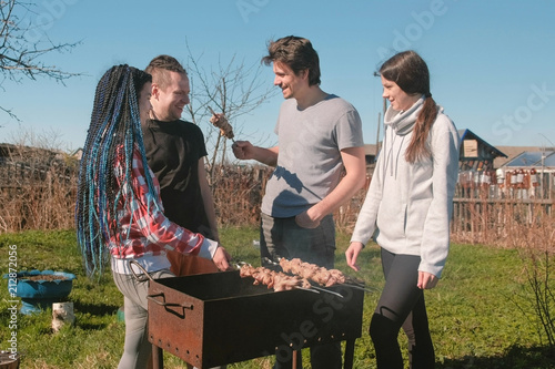 Group of young people friends Barbecue shashlik meat on top of charcoal grill on backyard. Talking and smiling together. photo