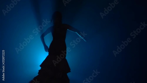 Woman dances flamenco movements . Light from behind. Smoke blue background. Slow motion