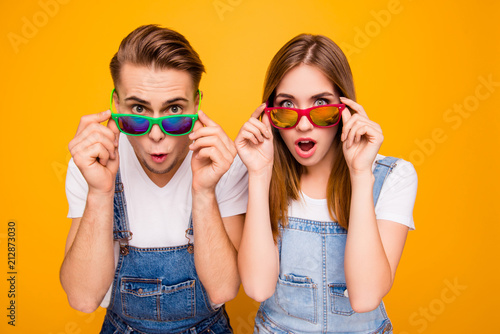 Beautiful cute adorable surprised couple putting colorful 3d spectacles down showing wow emotion over yellow background, isolated © deagreez