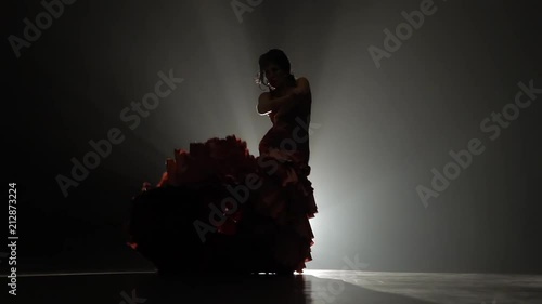 Girl is dancing with castanets and her leg is tugging at the tail of the dress. Light from behind. Smoke background. Slow motion