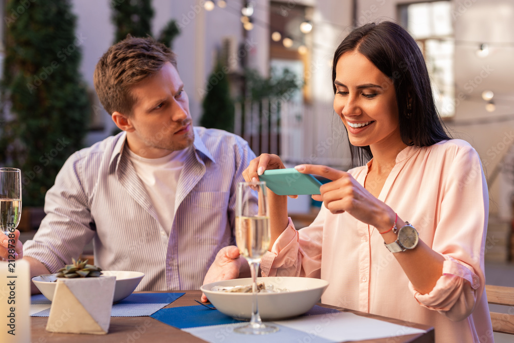 Surprised man. Handsome man feeling surprised while girlfriend taking pictures of her food during date Surprised man. Handsome man feeling surprised while girlfriend taking pictures of her food during date