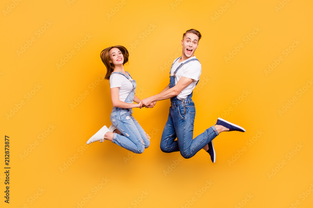 Full length portrait of beautiful attractive playful cheerful, comic couple in casual outfit, jeans, shirts jumping in the air on yellow background, isolated Full length portrait of beautiful attractive playful cheerful, comic couple in casual outfit, jeans, shirts jumping in the air on yellow background, isolated