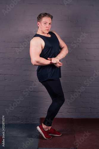 young handsome white man in black T-shirt posing with his own body on a black brick background. The idea of metabolism